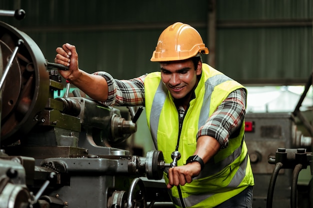 Hombre joven trabajador industrial que trabaja con la máquina de metal en la fábrica con muchos equipos