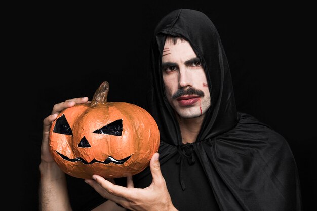 Hombre joven en traje de Halloween con calabaza decorativa