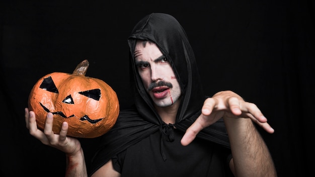 Hombre joven en traje de Halloween posando con Jack O&#39;Lantern