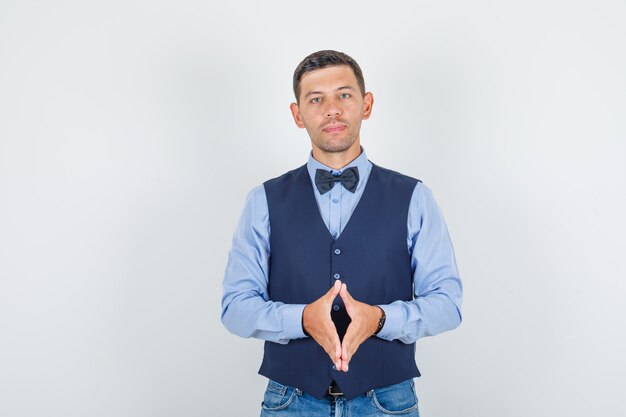 Hombre joven en traje, jeans manteniendo los dedos juntos y mirando esperanzado