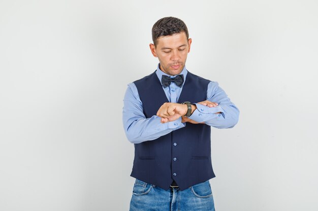 Hombre joven en traje, jeans mirando su reloj y mirando puntual