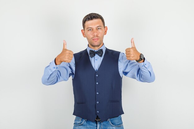 Hombre joven en traje, jeans mostrando los pulgares hacia arriba y mirando complacido