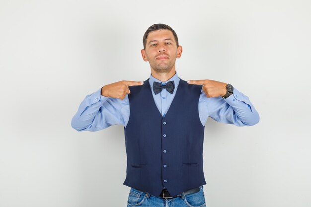 Hombre joven en traje, jeans mostrando su pajarita y mirando alegre