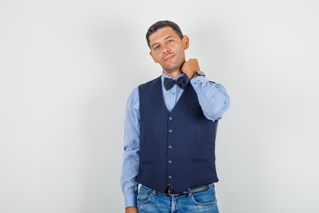 Hombre joven en traje, jeans posando mientras sostiene el cuello de la mano y luce elegante