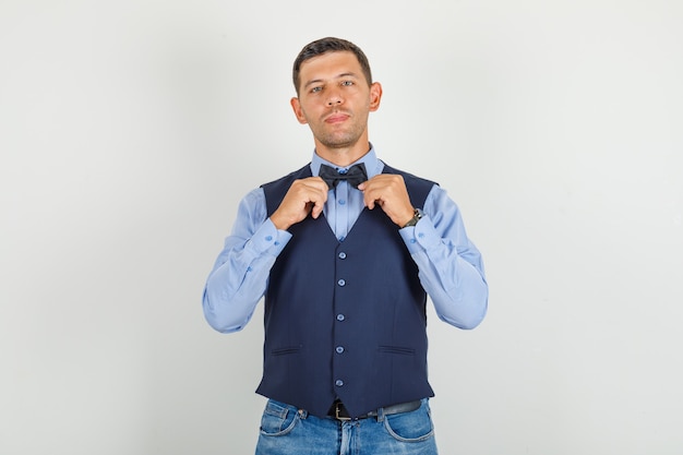 Hombre joven en traje, jeans posando sosteniendo pajarita