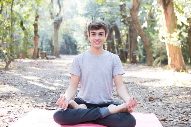 Hombre joven tranquilo sentado y meditando en una postura de yoga