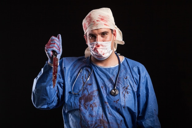 Hombre joven vestido con traje de médico para halloween sobre fondo negro. Retrato de médico con cara de maldad.