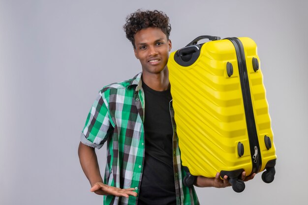 Hombre joven viajero afroamericano con maleta sonriendo alegremente, positivo y feliz