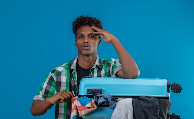 Hombre joven viajero afroamericano sosteniendo la maleta llena de ropa con aspecto aburrido y cansado