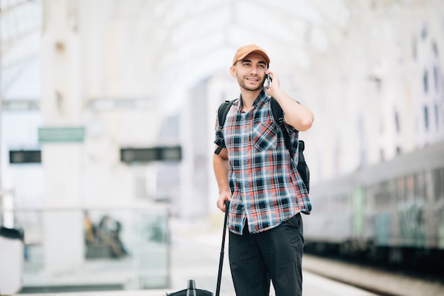 Hombre joven viajero hablando por teléfono en la estación de tren
