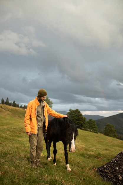 Hombre joven viajero de pie junto a un caballo