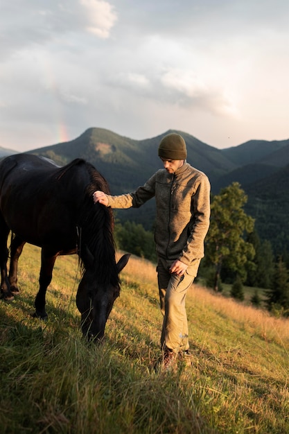 Hombre joven viajero de pie junto a un caballo