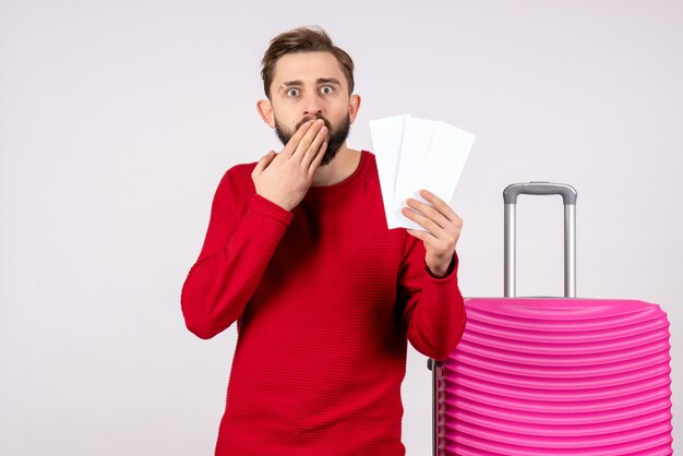 Hombre joven de vista frontal con bolsa rosa y sosteniendo boletos de avión en la pared blanca viaje vuelo viaje vacaciones turísticas emoción fotos