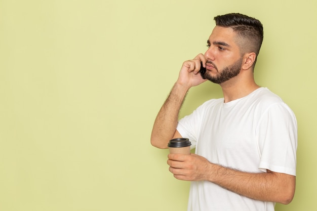 Un hombre joven de vista frontal en camiseta blanca con café hablando por teléfono