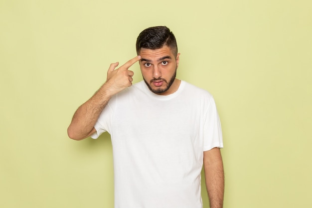 Un hombre joven de vista frontal en camiseta blanca con el dedo en la cabeza