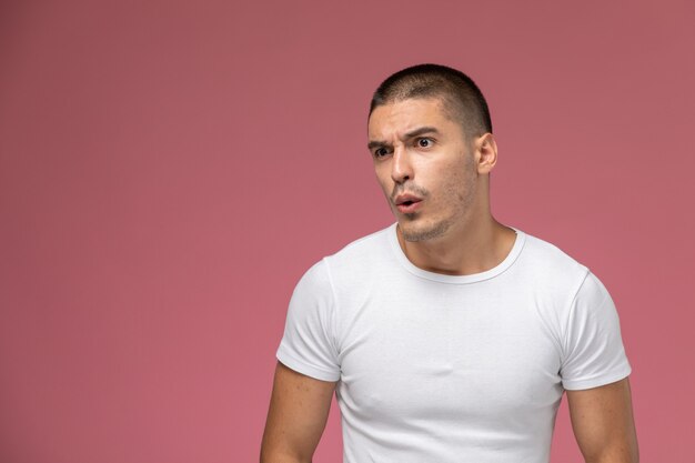 Hombre joven de vista frontal en camiseta blanca con expresión de sorpresa sobre fondo rosa