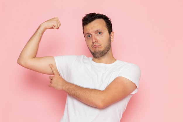 Un hombre joven de vista frontal en camiseta blanca flexionando sobre el escritorio rosa hombre color emoción pose