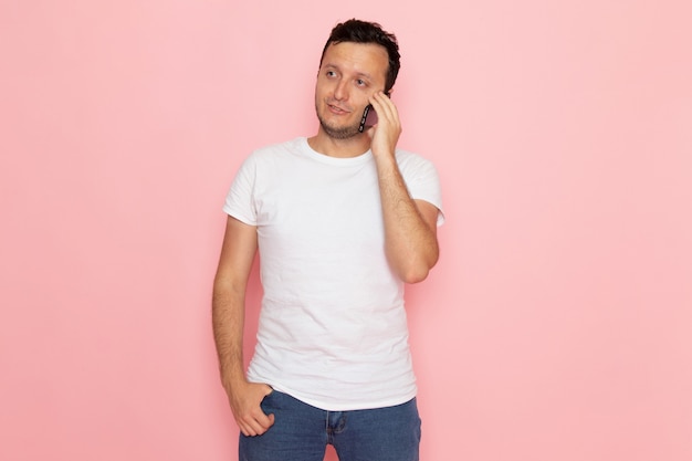 Un hombre joven de vista frontal en camiseta blanca hablando por teléfono en el escritorio rosa hombre color emoción pose
