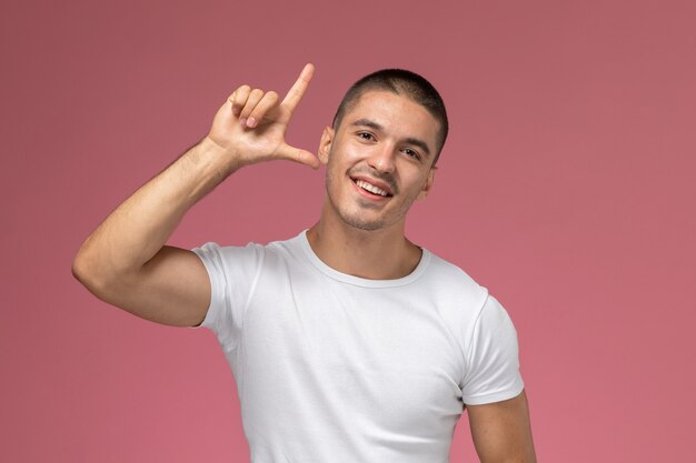 Hombre joven de vista frontal en camiseta blanca posando con el dedo levantado sobre fondo rosa