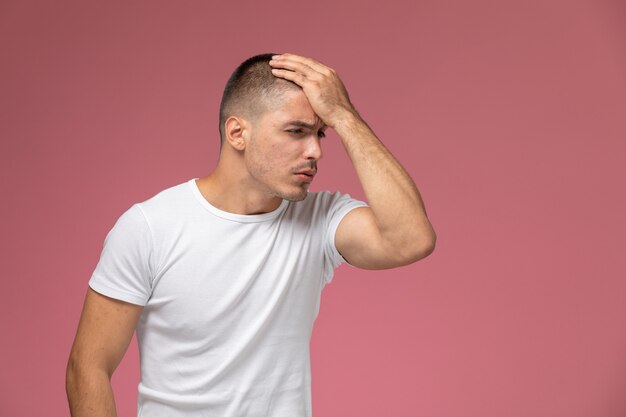 Hombre joven de vista frontal en camiseta blanca posando con expresión estresada sobre fondo rosa