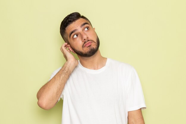 Un hombre joven de vista frontal en camiseta blanca posando con expresión de pensamiento