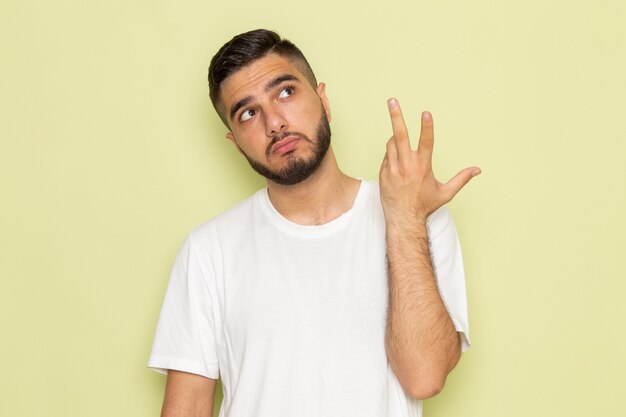 Un hombre joven de vista frontal en camiseta blanca posando y pensando