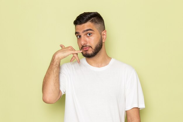 Un hombre joven de vista frontal en camiseta blanca que muestra la señal de llamada telefónica