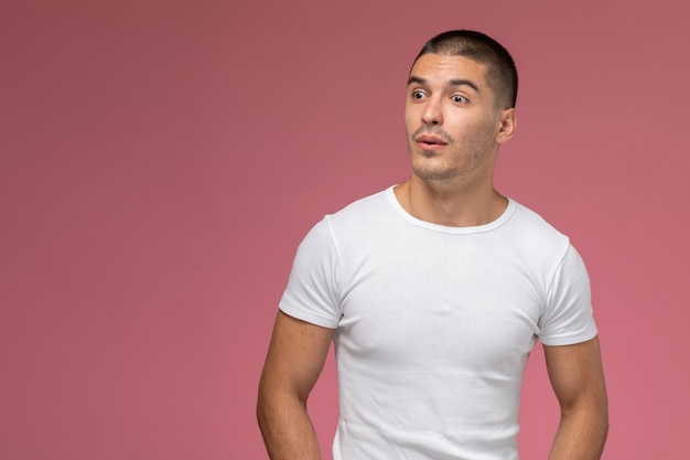 Hombre joven de vista frontal en camiseta blanca simplemente posando sobre el fondo rosa