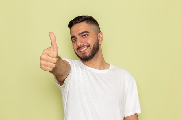 Un hombre joven de vista frontal en camiseta blanca sonriendo posando con signo similar