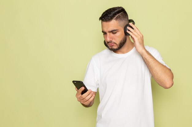 Un hombre joven de vista frontal en camiseta blanca sosteniendo el teléfono y escuchando música