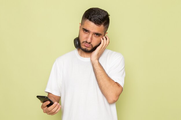 Un hombre joven de vista frontal en camiseta blanca sosteniendo el teléfono y escuchando música