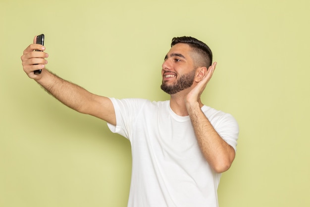 Un hombre joven de vista frontal en camiseta blanca tomando un selfie con sonrisa