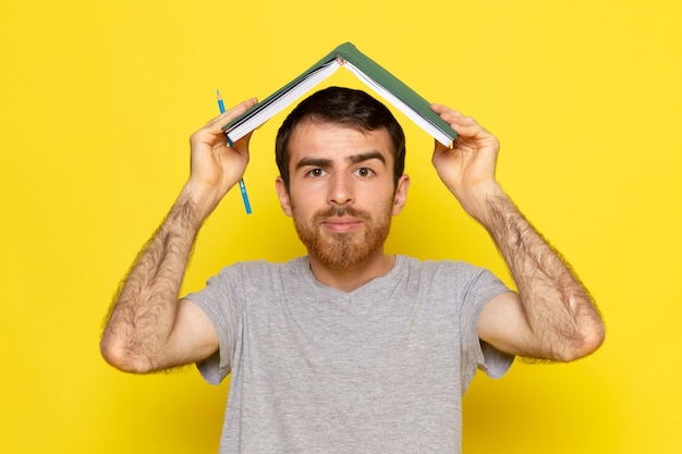 Un hombre joven de vista frontal en camiseta gris con cuaderno en la pared amarilla hombre color modelo emoción ropa