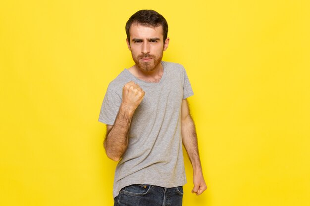 Un hombre joven de vista frontal en camiseta gris con expresión encantada en la pared amarilla hombre expresión emoción modelo de color