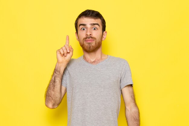 Un hombre joven de vista frontal en camiseta gris con una expresión de idea en el modelo de color de emoción de expresión de hombre de pared amarilla