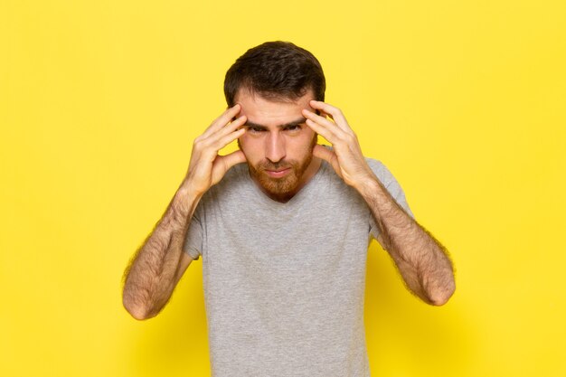 Un hombre joven de vista frontal en camiseta gris con expresión de pensamiento en el modelo de color de expresión de hombre de pared amarilla