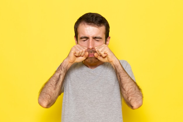 Foto gratuita un hombre joven de vista frontal en camiseta gris falso llorando en la pared amarilla hombre color modelo emoción ropa