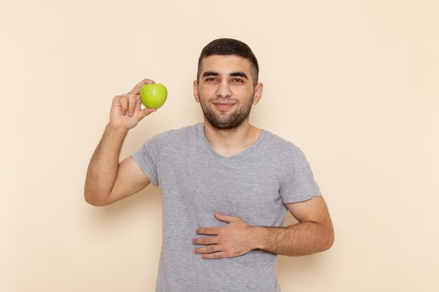 Foto gratuita hombre joven de vista frontal en camiseta gris con manzana verde en beige