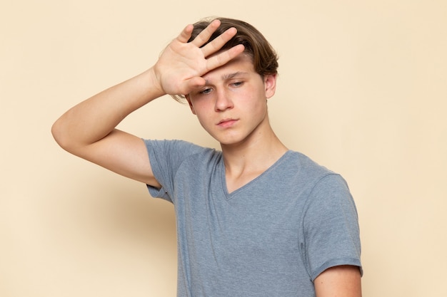 Un hombre joven de vista frontal en camiseta gris posando con expresión deprimida