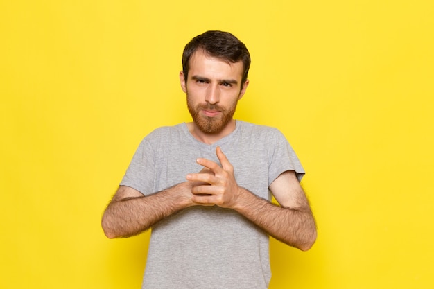 Foto gratuita un hombre joven de vista frontal en camiseta gris posando en la pared amarilla hombre expresión emoción modelo de color