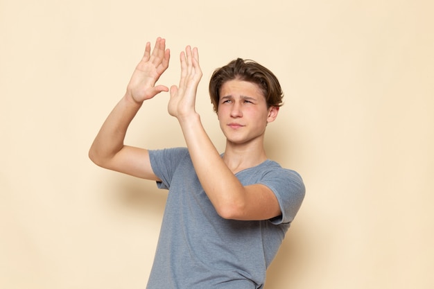 Un hombre joven de vista frontal en camiseta gris posando con precaución