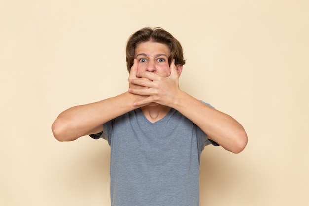 Foto gratuita un hombre joven de vista frontal en camiseta gris posando tapándose la boca