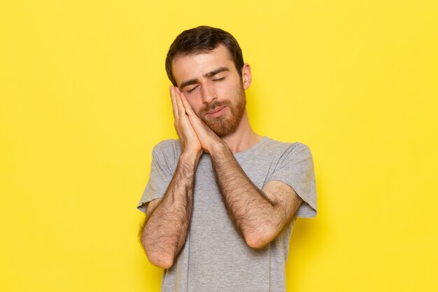 Un hombre joven de vista frontal en camiseta gris con pose para dormir en la pared amarilla modelo de color del hombre