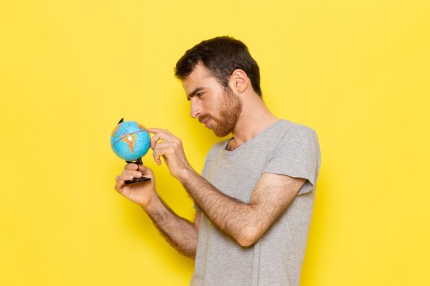 Un hombre joven de vista frontal en camiseta gris sosteniendo un pequeño globo en la pared amarilla hombre color modelo emoción ropa