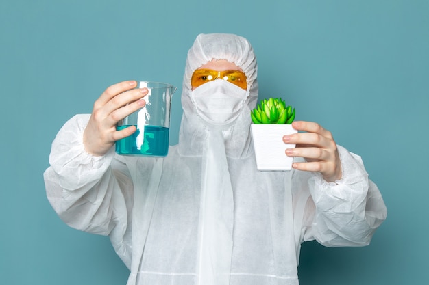 Un hombre joven de vista frontal en traje blanco especial que sostiene la solución y la planta en la pared azul traje de hombre peligro equipo especial color