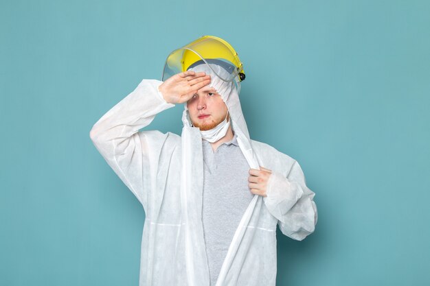 Un hombre joven de vista frontal en traje especial blanco y casco especial amarillo en la pared azul traje de hombre peligro color de equipo especial