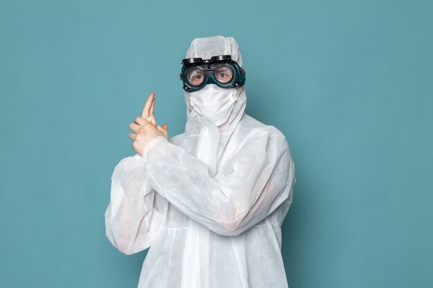 Un hombre joven de vista frontal en traje especial blanco con gafas de sol especiales en la pared azul traje de hombre peligro equipo especial color