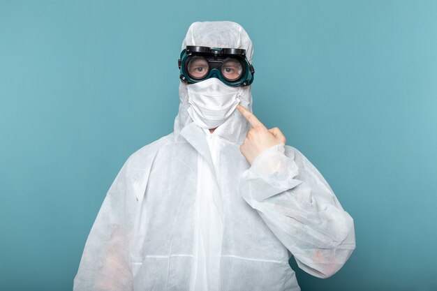 Un hombre joven de vista frontal en traje especial blanco y gafas de sol protectoras únicas en la pared azul traje de hombre peligro color de equipo especial