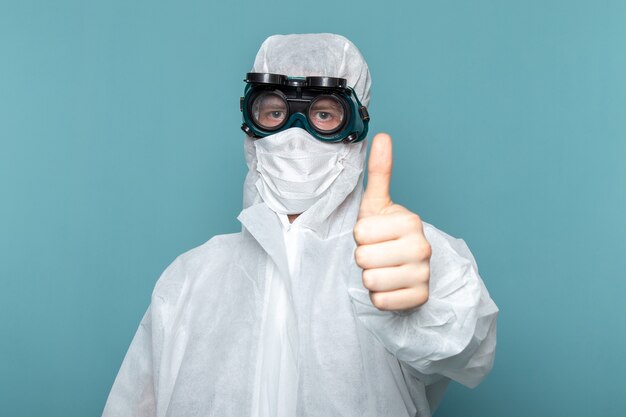 Un hombre joven de vista frontal en traje especial blanco y gafas de sol protectoras únicas en la pared azul traje de hombre peligro color de equipo especial