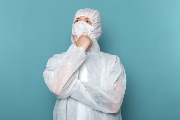 Foto gratuita un hombre joven de vista frontal en traje especial blanco con máscara protectora estéril pensando en la pared azul traje de hombre peligro equipo especial color